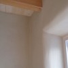 Soft curves around a clay plastered window meet an exposed ceiling beam.