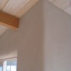 A clay plastered wall with exposed ceiling beams.